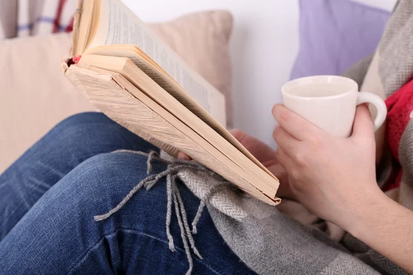 Frau sitzt auf Sofa, liest Buch und trinkt Kaffee oder Tee, Nahaufnahme — Stockfoto