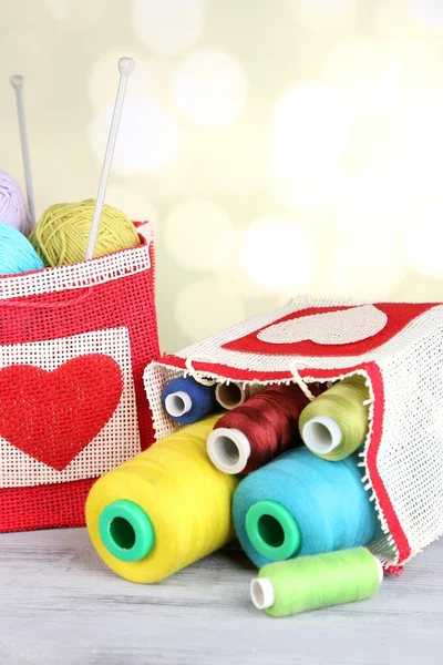 Bags with bobbins of colorful thread and woolen balls on wooden table, on light background — Stock Photo, Image