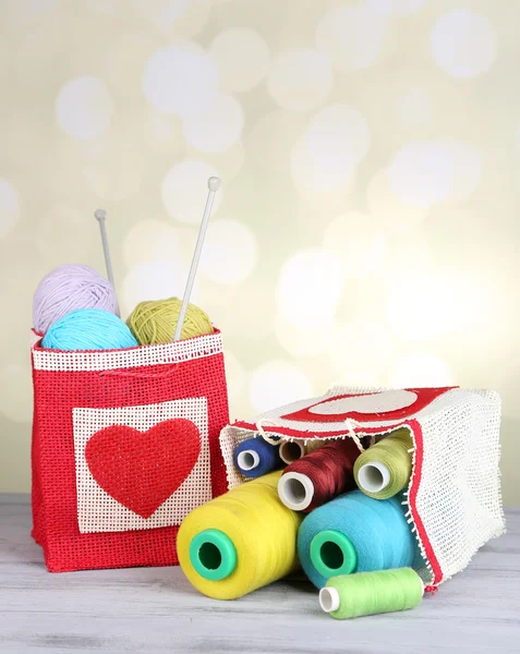 Bags with bobbins of colorful thread and woolen balls on wooden table, on light background — Stock Photo, Image