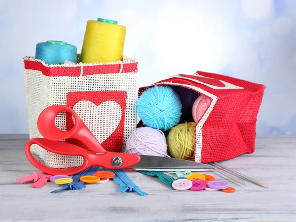 Bags with bobbins of colorful thread and woolen balls on wooden table, on light background — Stock Photo, Image