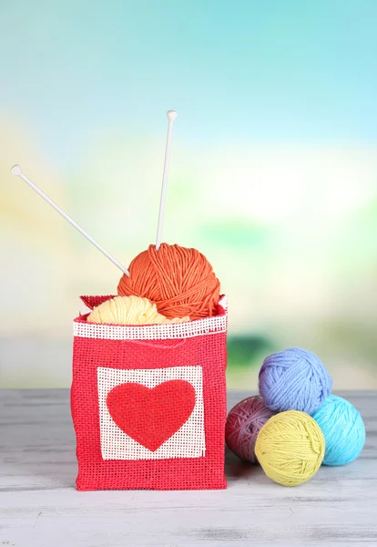 Woolen balls of yarn in rustic craft bag, om wooden table, on light background — Stock Photo, Image