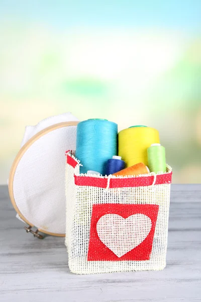 Colorful bobbins of thread  in bag, on wooden table, on light background — Stock Photo, Image