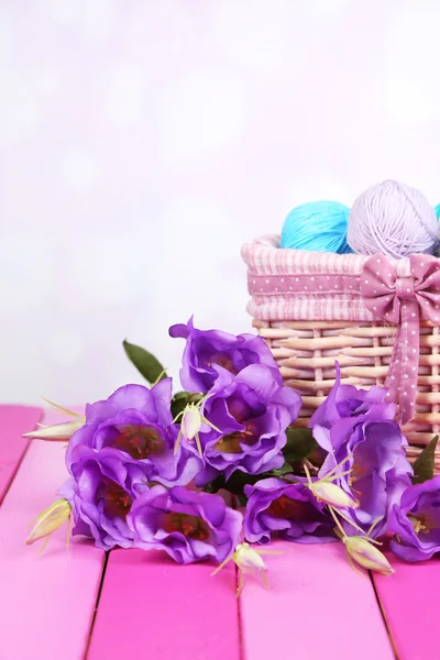 Purple artificial eustoma and woolen balls of yarn in basket on light background — Stock Photo, Image