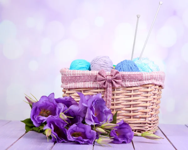 Purple artificial eustoma and woolen balls of yarn in basket on light background — Stock Photo, Image