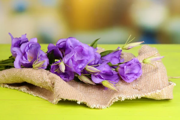 Purple artificial eustoma on sackcloth on color wooden  table, on bright background — Stock Photo, Image