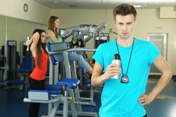 Unga tränare och kvinnans bedriver simulator i gym — Stockfoto