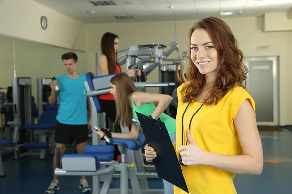Jonge trainer en dames die zich bezighouden met simulator in gym — Stockfoto