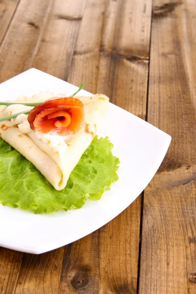 Pancake con salmone e maionese, cipolla verde, su piatto, su fondo di legno — Foto Stock