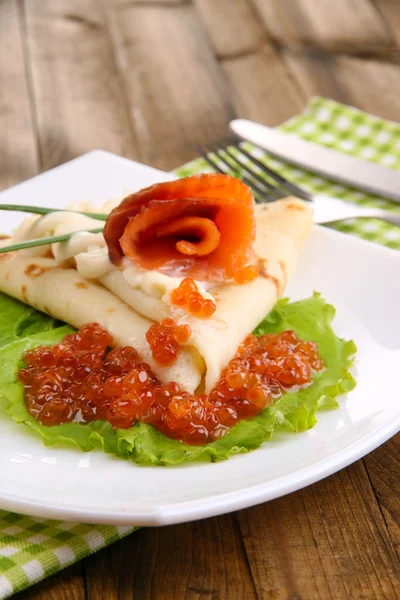 Panqueque con salmón, caviar rojo y mayonesa, cebolla verde, en plato, servilleta de color, sobre fondo de madera —  Fotos de Stock