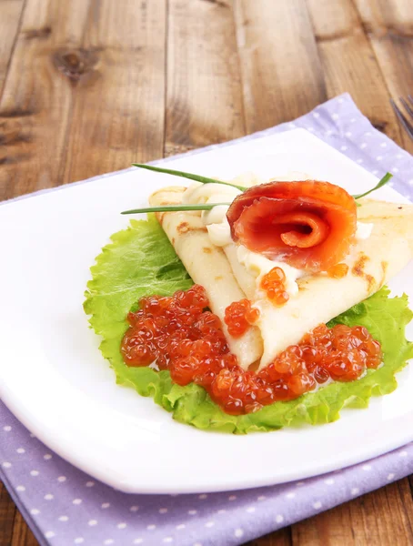 Pancake with salmon, red caviar and mayo, green onion, on plate, on color napkin, on wooden background — Stock Photo, Image