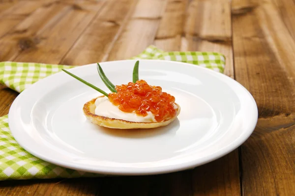 Panqueca com caviar vermelho e maionese, cebola verde, na placa, no guardanapo de cor, no fundo de madeira — Fotografia de Stock