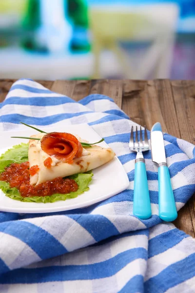 Pannenkoek met rode kaviaar, zalm en mayo, groene ui, op plaat, op kleur servet, op houten tafel, op lichte achtergrond — Stockfoto