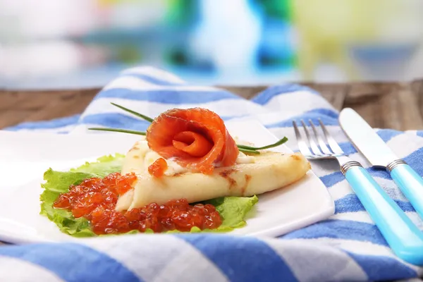 Pancake with red caviar, salmon and mayo, green onion, on plate, on color napkin, on wooden  table, on bright background — Stock Photo, Image