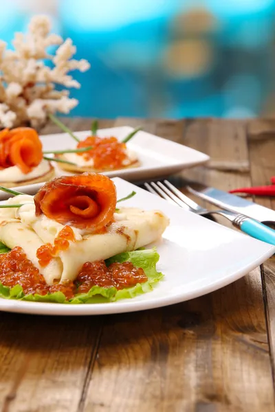 Frittelle con caviale rosso, salmone e maionese, cipolla verde, su piatto, su tavolo di legno, su sfondo brillante — Foto Stock