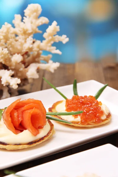 Frittelle con caviale rosso, salmone e maionese, cipolla verde, su piatto, su tavolo di legno, su sfondo brillante — Foto Stock