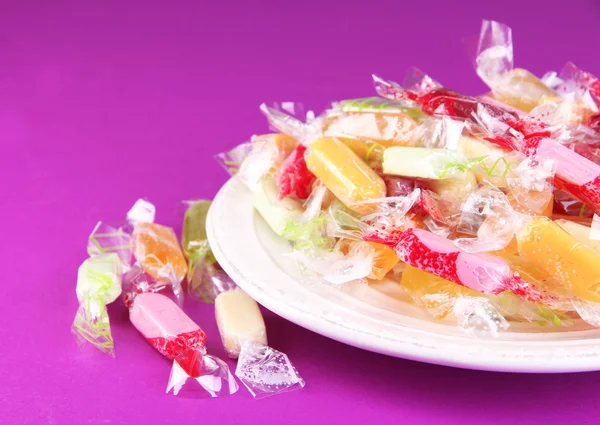 Tasty candies on plate on purple background — Stock Photo, Image