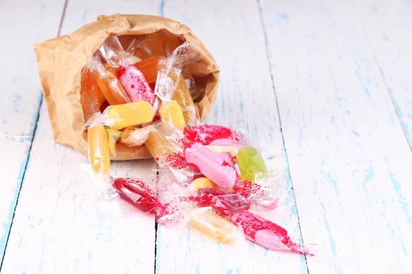 Tasty candies in paper bag on wooden background — Stock Photo, Image