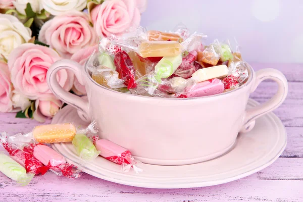 与花在明亮的背景上桌上的碗里的美味糖果 — 图库照片