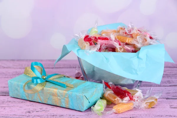 Tasty candies in vase with present  on table on bright background — Stock Photo, Image