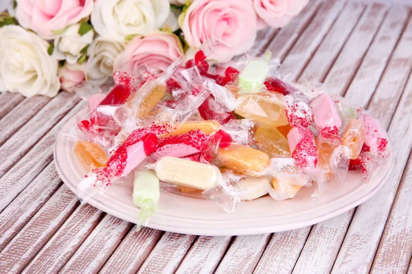 Sabrosos caramelos en plato con flores sobre fondo de madera —  Fotos de Stock