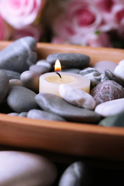 Cuenco de madera con piedras de spa y velas sobre mesa de madera, sobre fondo de flores — Foto de Stock