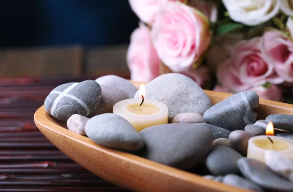 Komposition mit Wellness-Steinen und Kerzen in Holzschale, in der Nähe von Blumen auf hellem Hintergrund — Stockfoto