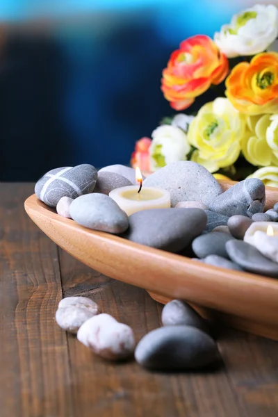 Composizione con pietre termali e candele in ciotola di legno, vicino a fiori su sfondo luminoso — Foto Stock