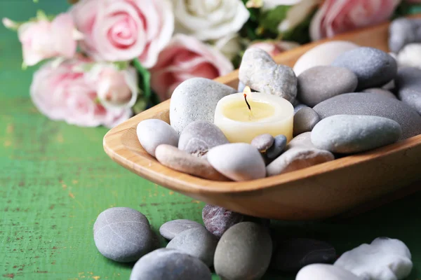 Wooden bowl with spa stones and candles on wooden  table, on flowers background — Stock Photo, Image