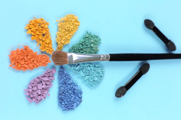 Rainbow crushed eyeshadow in shape of flower on blue background — Stock Photo, Image