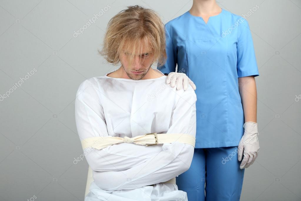 Mentally ill man in strait-jacket on gray background