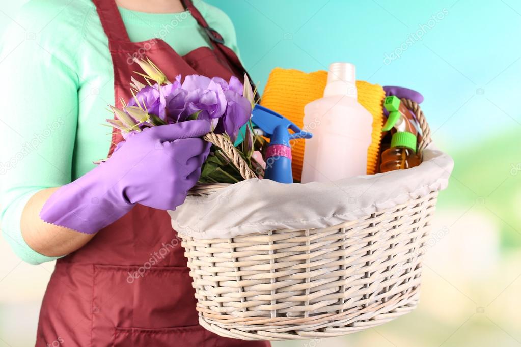 Housewife holding basket with cleaning equipment on bright background. Conceptual photo of spring cleaning. 