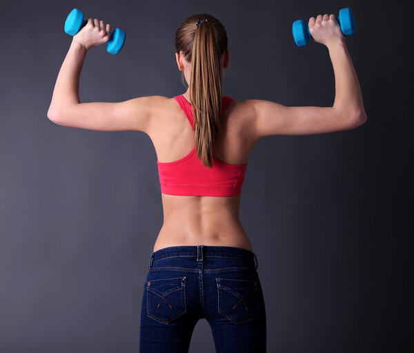 Young beautiful fitness girl exercising with dumbbells, close-up, on gray background