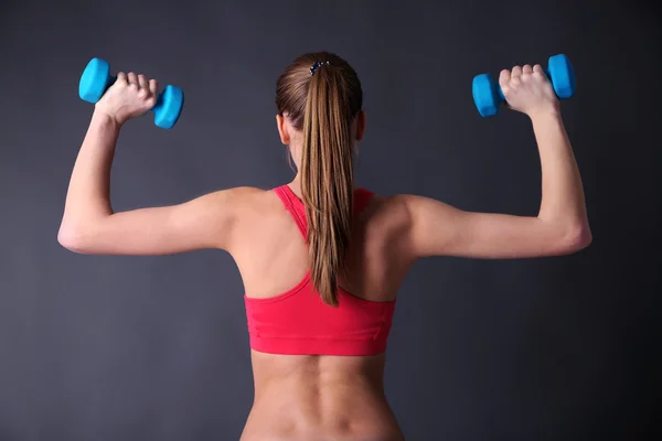 Joven hermosa chica de fitness haciendo ejercicio con pesas, primer plano, sobre fondo gris —  Fotos de Stock