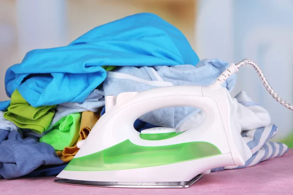 Eisen und Stapel bunter Kleidung auf dem Tisch vor hellem Hintergrund — Stockfoto