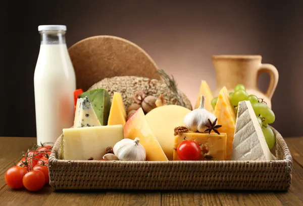 Basket with tasty dairy products on wooden tray, on dark background — Stock Photo, Image