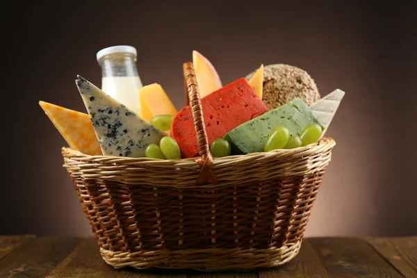 Basket with tasty dairy products on wooden table, on dark background — Stock Photo, Image