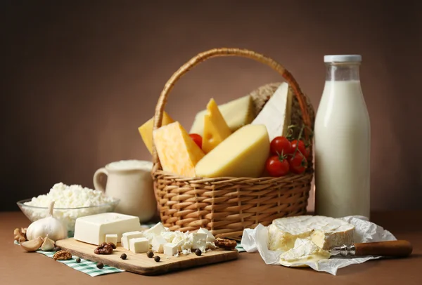 Basket with tasty dairy products on wooden table, on dark brown background — Stock Photo, Image