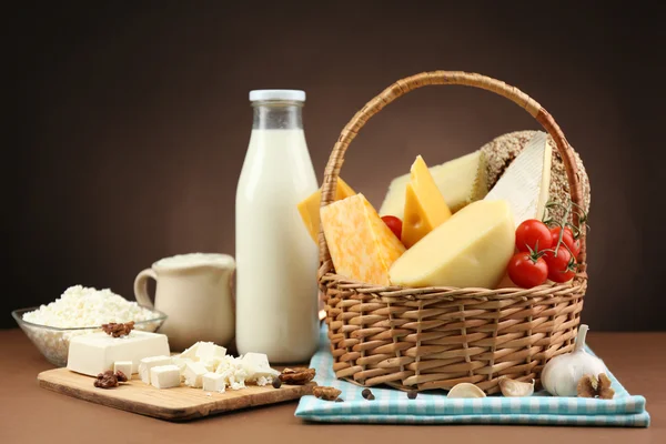 Basket with tasty dairy products on wooden table, on dark brown background — Stock Photo, Image