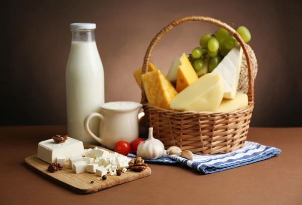 Корзина с вкусными молочными продуктами на деревянном столе, на темно-коричневом фоне — стоковое фото