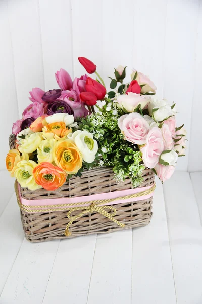 Beautiful flowers in wicker basket, on color wooden background — Stock Photo, Image