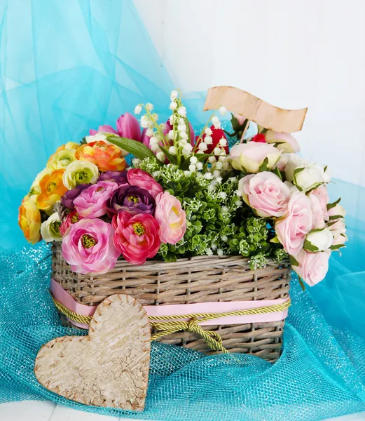 De belles fleurs dans un panier en osier, sur un tissu de couleur et un fond en bois — Photo