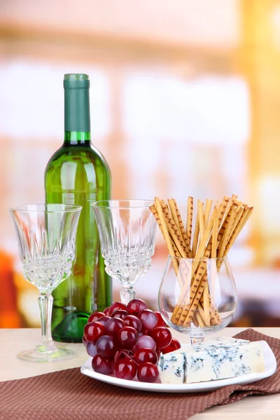 Formaggio, uva e bastoncini di pane sul piatto sul tavolo di legno, su sfondo luminoso — Foto Stock