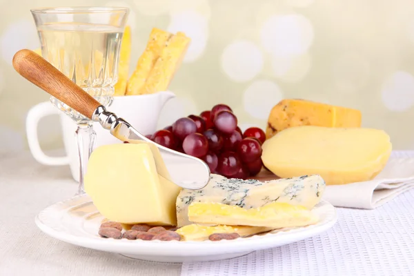 Assorted cheese plate, cocoa beans and grape on tablecloth background, close-up — Stock Photo, Image