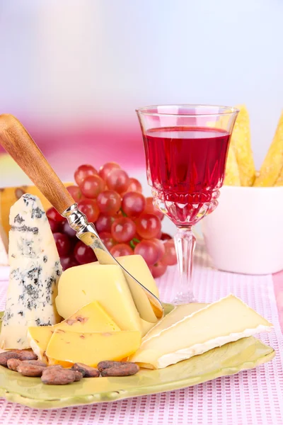 Placa de queso surtido, copa de uva y vino en la mesa, sobre fondo claro — Foto de Stock