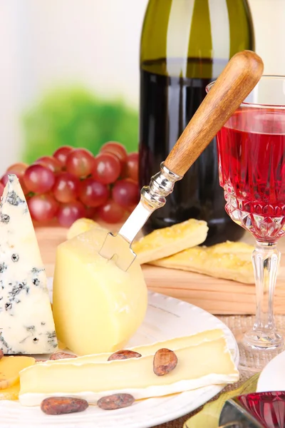 Prato de queijo sortido, uva e copo de vinho na mesa, no fundo claro — Fotografia de Stock