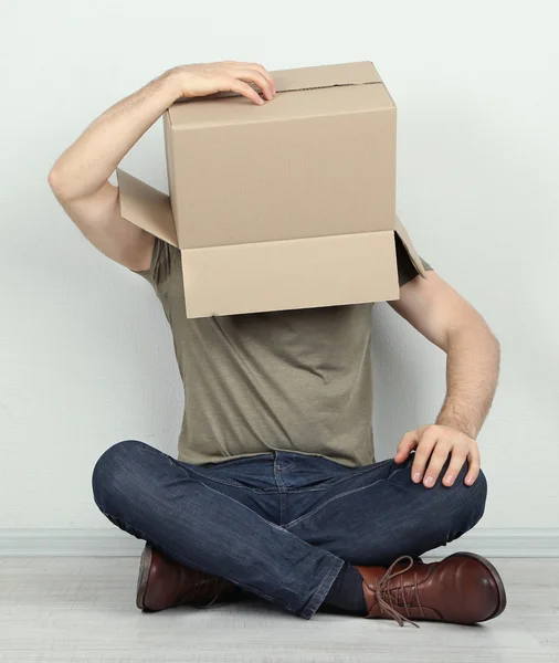 Muž s krabici na hlavě sedí na podlaze u zdi — Stock fotografie