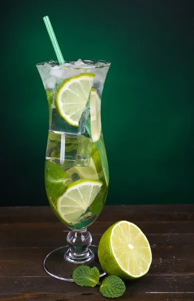 Glass of cocktail with lime and mint on table on dark green background — Stock Photo, Image