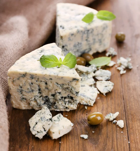 Schmackhafter Blauschimmelkäse mit Oliven und Basilikum, auf Holztisch — Stockfoto