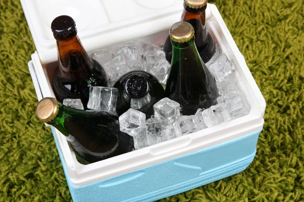 Pecho de hielo lleno de bebidas en botellas sobre fondo de alfombra de color —  Fotos de Stock