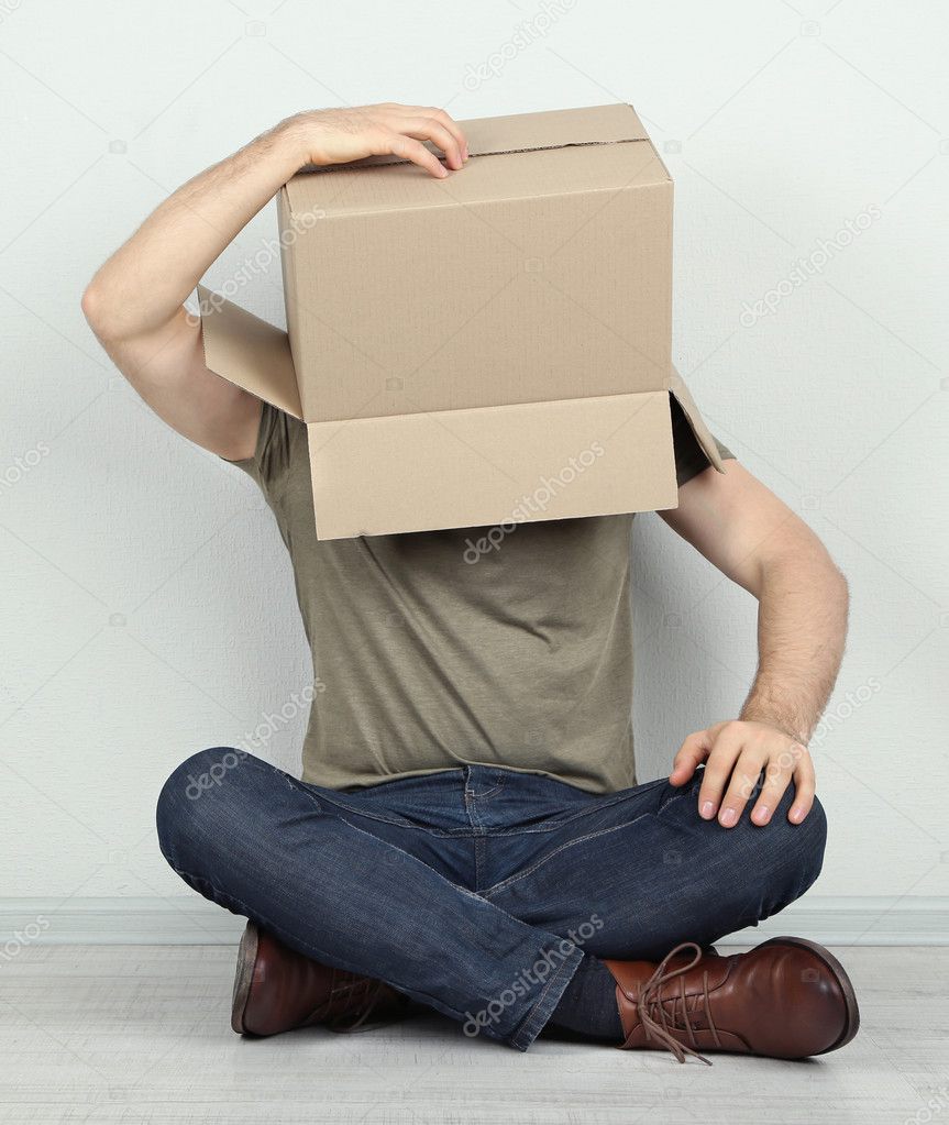 Man with cardboard box on his head sitting on floor near wall